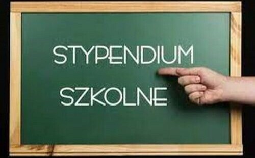 Tablica szkolna z&nbsp;obramowaniem drewnianym- sosnowym z&nbsp;tłem koloru zielonego. Na środku tablicy szkolnej umieszczony napis biały pt. &bdquo;Stypendium szkolne&rdquo;, na&nbsp;kt&oacute;ry pokazuje palec wskazujący- przy  jednoczesnym złożeniu innych palc&oacute;w. 